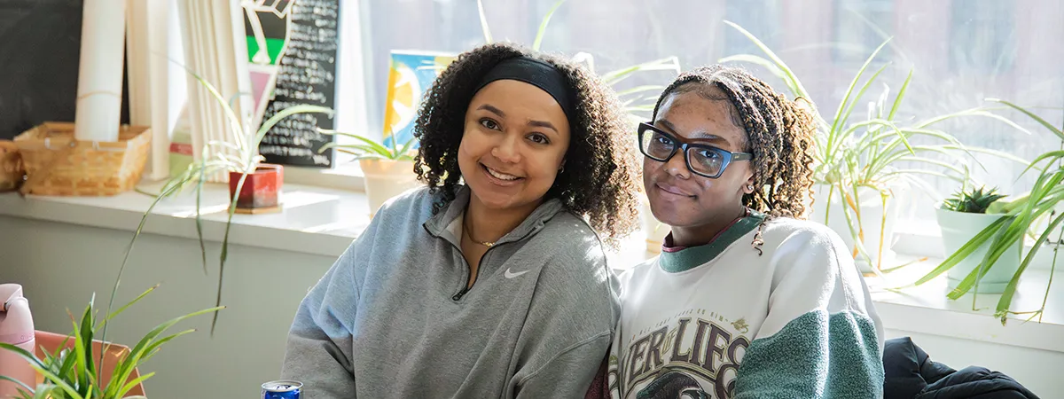 Two students smile in front of a window